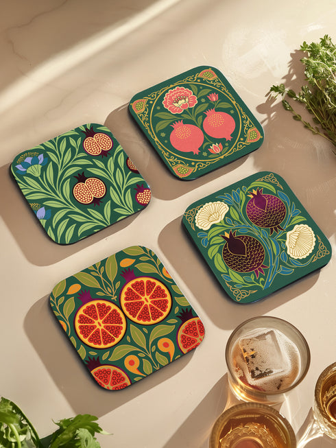 Set of four square drinking coasters featuring rich, dark green botanical illustration with highly detailed Pomegranate fruits and sliced cross-sections. The ornate pattern utilizes deep crimson, opulent gold, and ivory tones, strongly reflecting the stylized Art Nouveau period aesthetic and William Morris textile designs. Crafted from durable, resilient masonite hardboard, this luxury item features a protective high-gloss finish and a non-slip cork base.